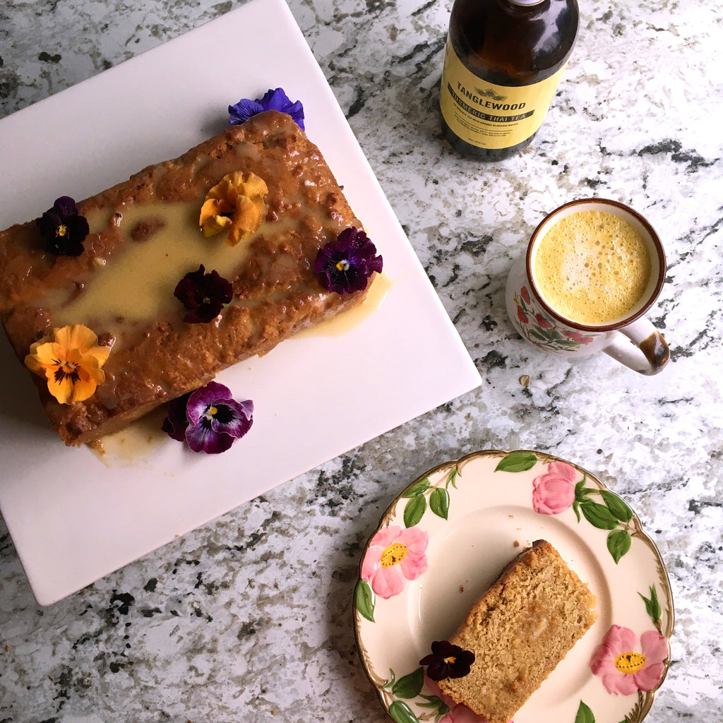A bottle of Turmeric Tea with a finishedVegan Lemon Loaf garnished with pansies. 