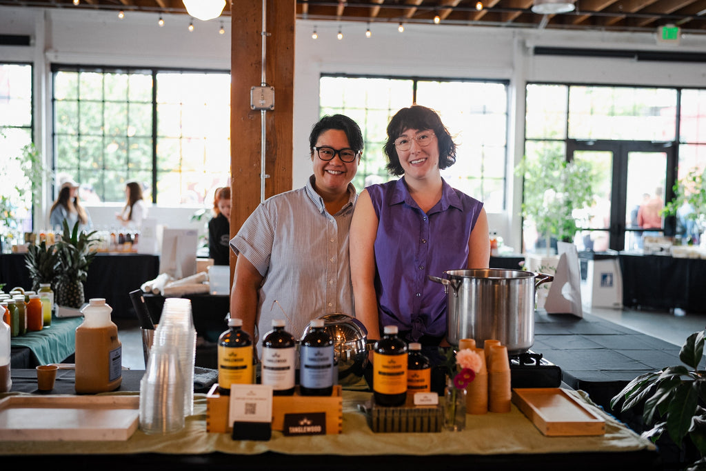 Misty and Ro at the Veganizer Event in front of Tanglewood Chai, Lavender Fog and Hot Buttered Yam.